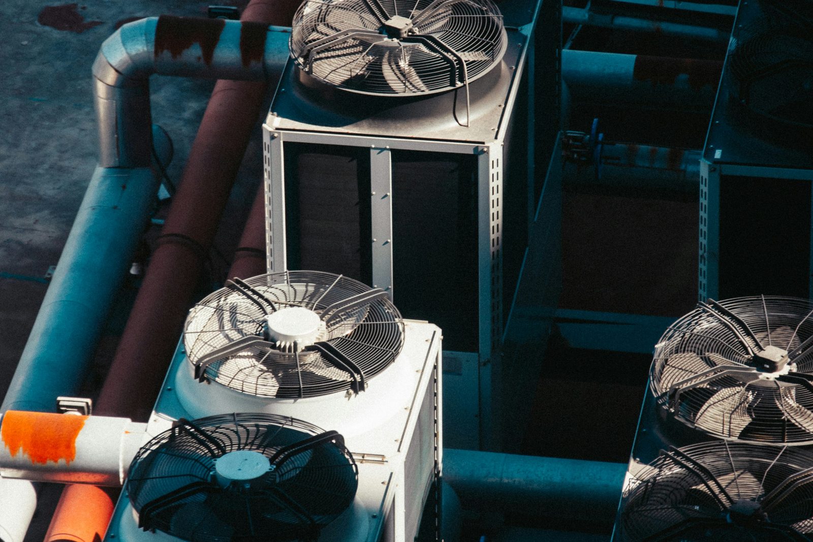 Four rooftop condenser units seen from above, fan guards and coil panels crowded in among painted pipe runs