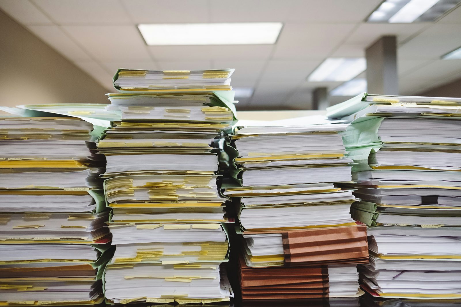 Deep stacks of paper files bristling with index tabs, filling an office desk